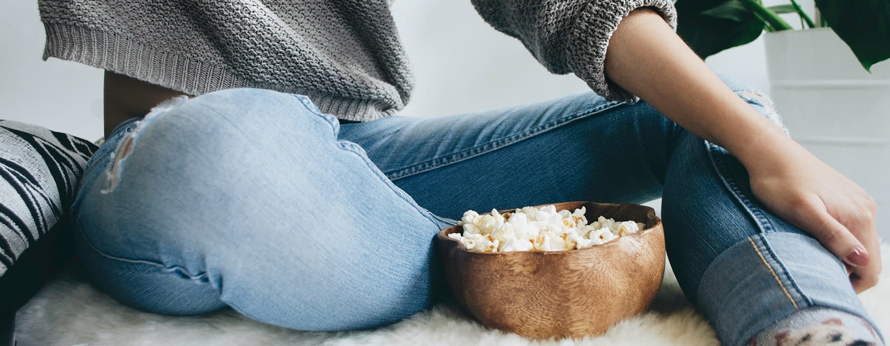 lifestyle image of a person sitting on a pillow while eating out of a wooden bowl of popcorn